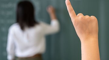A pupil speaks up while the teacher writes on the blackboard. / Photo: Marijan Murat/dpa/Symbolic image