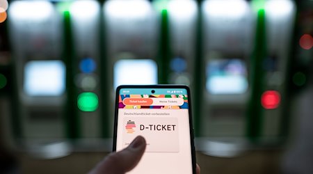 A man holds a cell phone, on which the "D-Ticket" can be purchased, in front of ticket machines at the main station / Photo: Fabian Strauch/dpa/Archivbild